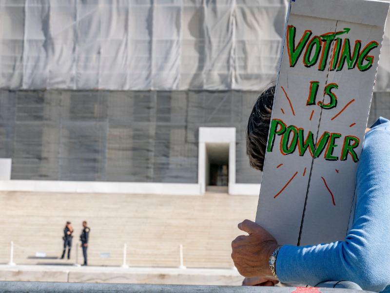 A person outside the Supreme Court holds a sign that says "Voting is Power"