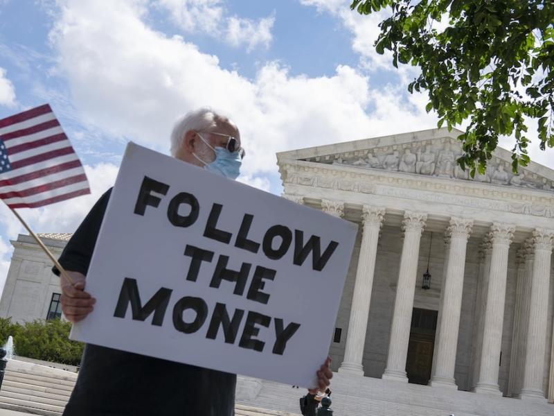 A man holds a sign in front of the Supreme Court that reads "Follow the Money"